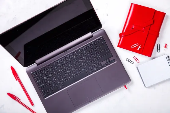 Laptop with red notebook and office supplies on white desk