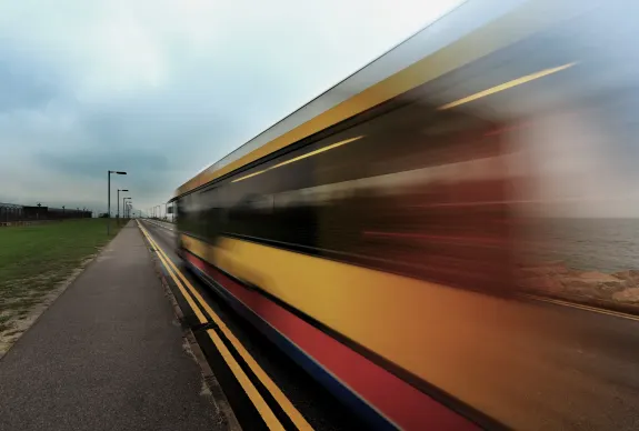 Yellow train with motion blur traveling along seaside road on a cloudy day