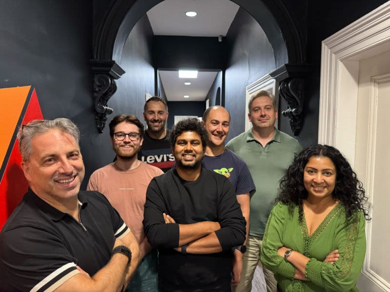 A diverse team of seven people smiling in an office hallway.