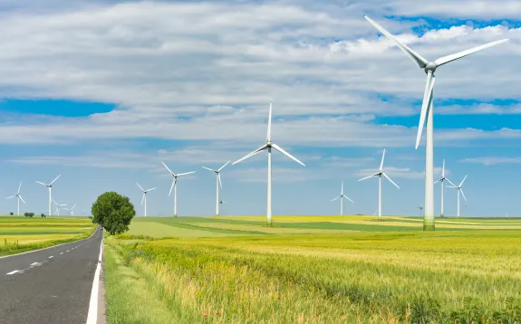Wind turbines in a green field under a blue sky with clouds.