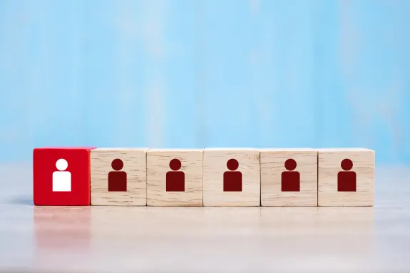 Red block with white icon among wooden cubes with brown icons on a blue background.