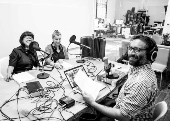 Three people recording a podcast at a table with microphones and headphones.