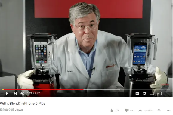 Person in lab coat holding blenders with smartphones inside for a blending demonstration.