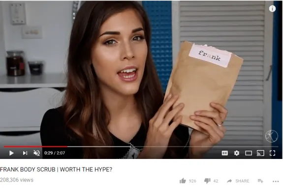 Woman holding Frank Body Scrub pouch during a review video.