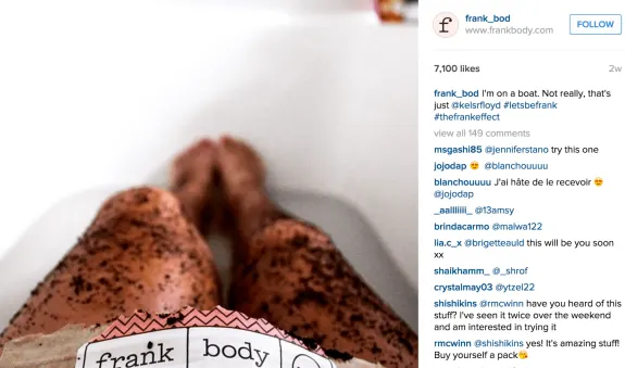 Person with coffee scrub on legs in a bath holding frank body product.