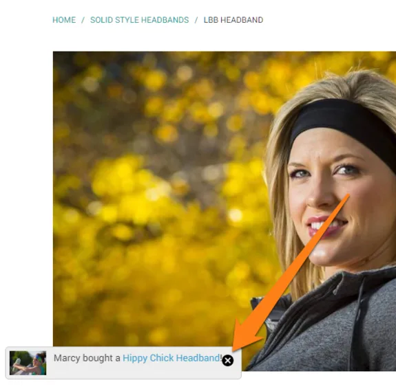 Woman wearing a black headband outdoors with fall leaves in the background.