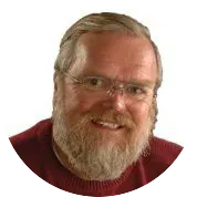 Man with glasses wearing a red sweater, smiling against white background.