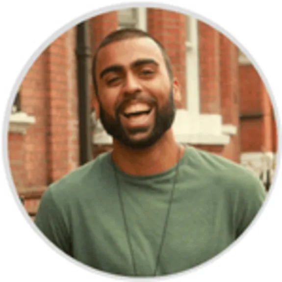 Man in green shirt smiling against brick wall background.