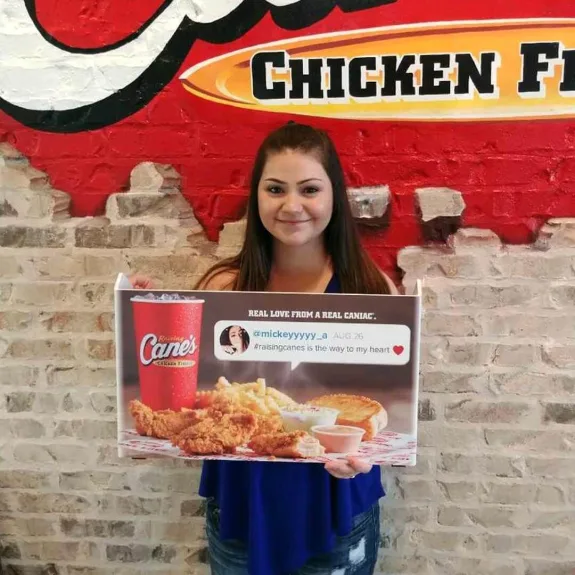 Woman holding Raising Cane's sign featuring chicken fingers and drink