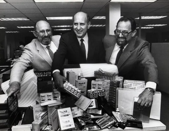 Three businessmen in suits smiling with office supplies on a desk in a vintage office.
