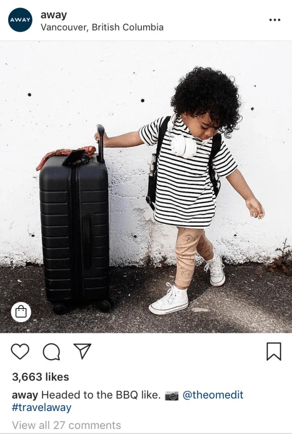Child in striped shirt with suitcase and headphones standing outdoors.