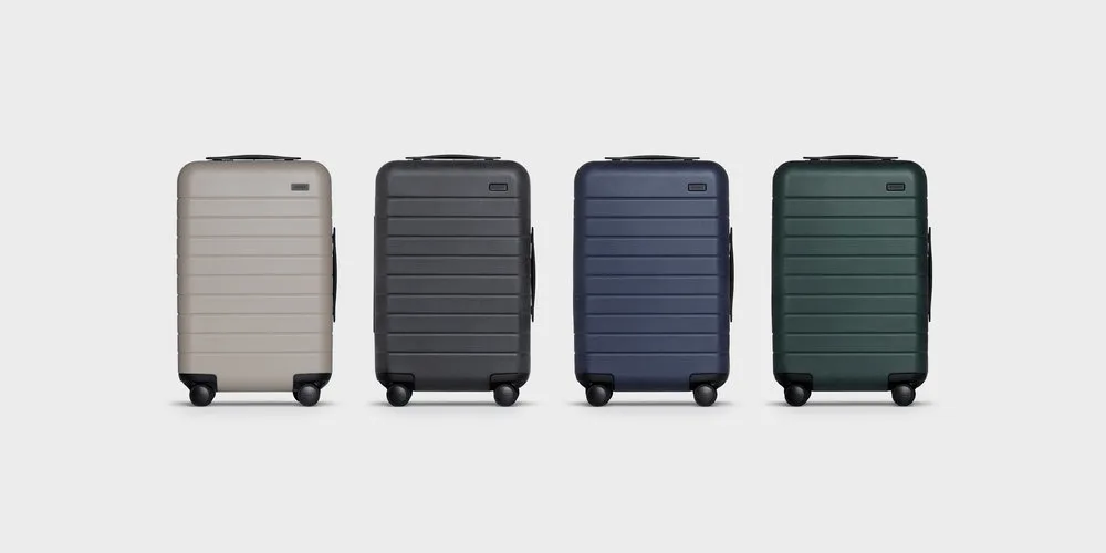 Set of four hard shell suitcases in beige, black, blue, and green on gray background.