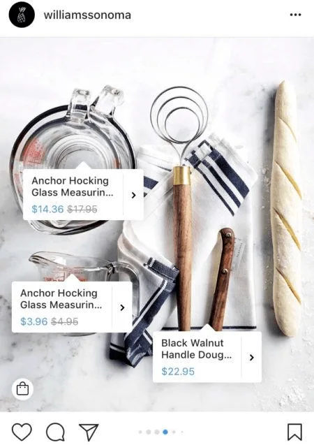 Kitchen utensils including measuring cups, dough whisk, and baguette on a white surface.