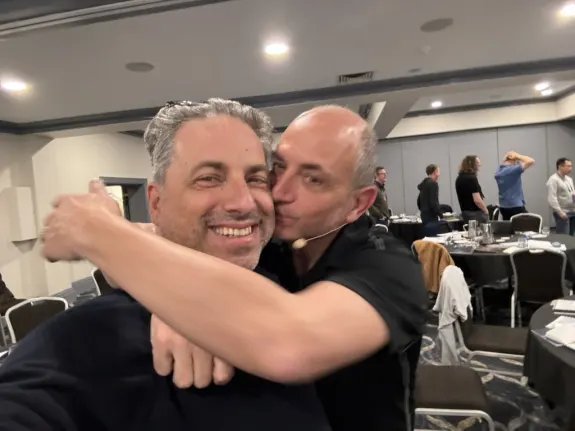 Two men hugging and smiling at a conference room event.