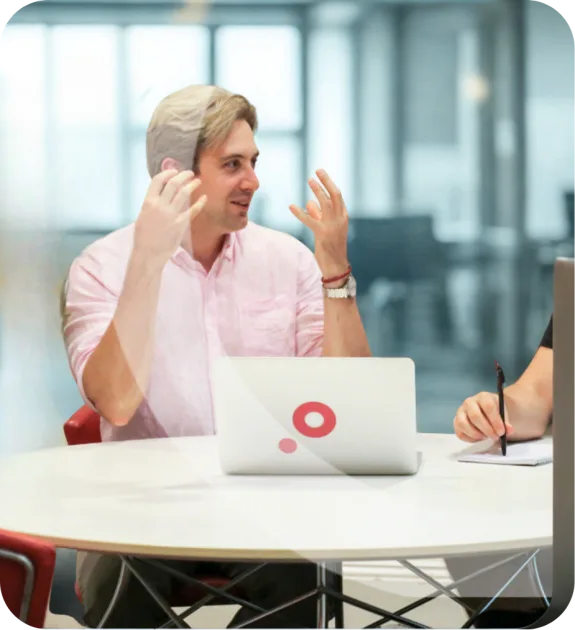 Two people discussing at a round table with a laptop in an office setting.