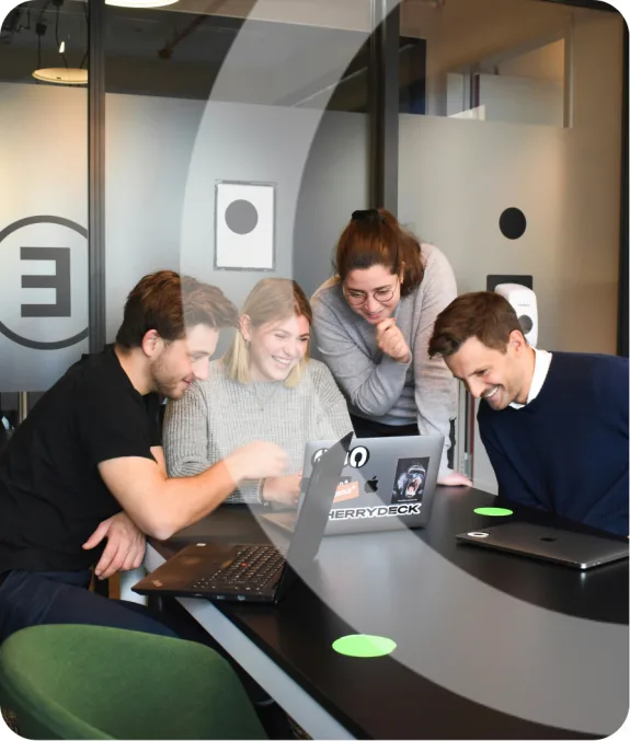 Group of four colleagues collaborating at a table with laptops in an office setting.